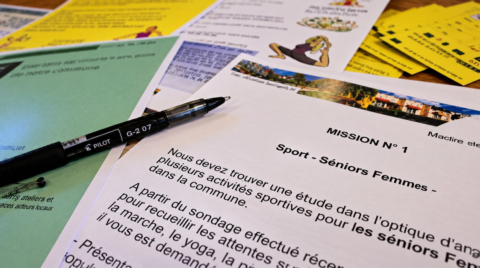 Des feuilles imprimées colorées et un stylo noir sont posés sur une table, avec un texte trop petit pour être lu.