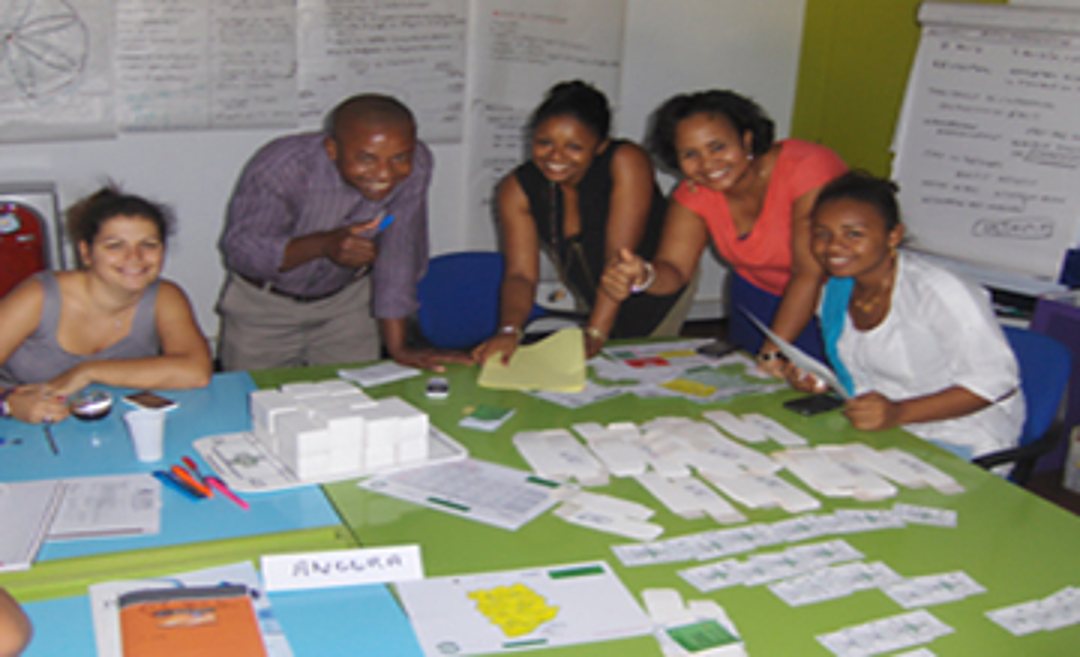 Cinq personnes souriantes travaillent ensemble autour d'une table verte couverte de cartes et de feuilles lors d'un atelier, avec des affiches en arrière-plan.