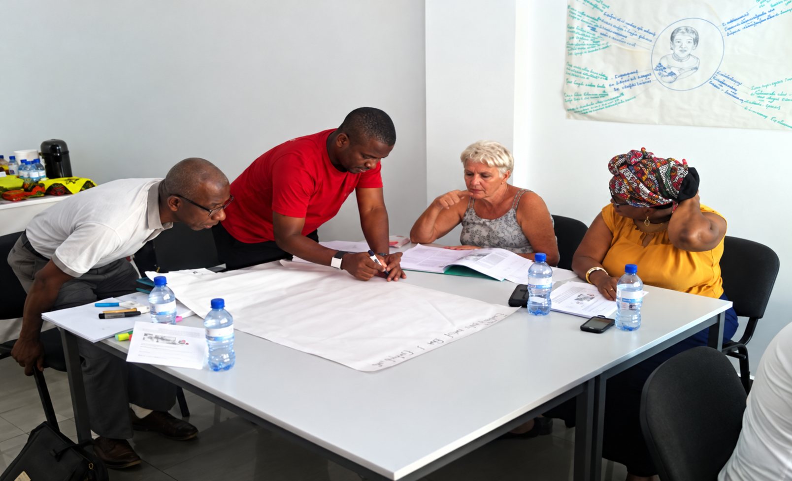 Quatre personnes sont réunies autour d'une table blanche couverte de grandes feuilles de papier et de bouteilles d'eau, lors d'un atelier de travail.